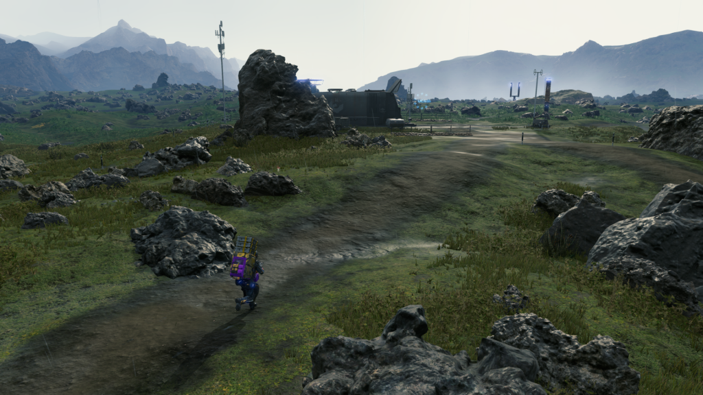 Image description: The protagonist treads along a worn dirt path, surrounded by craggy fields as he approaches a high tech shelter.